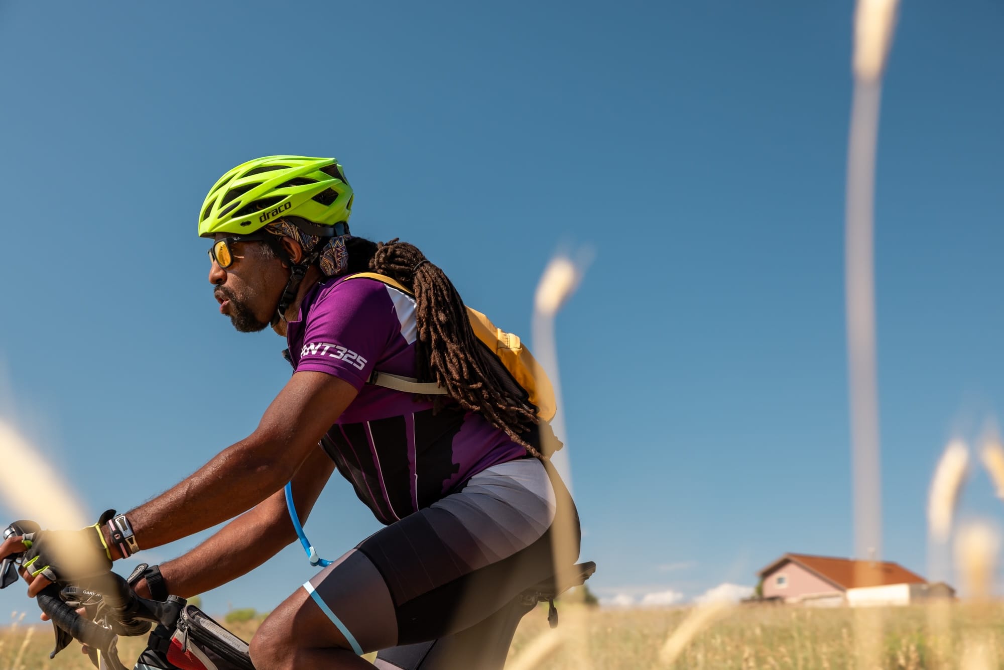 A rider with long braids rides through the Colorado plains during FoCo Fondo. He wears a purple jersey and dayglo yellow helmet.