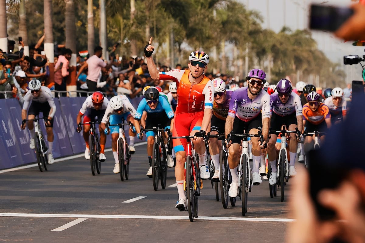 Cameron Scott leads the peloton across the finish line. He holds a single finger up to celebrate his victory.
