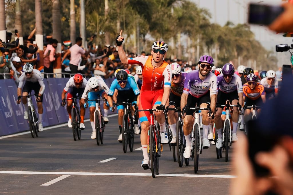 Cameron Scott leads the peloton across the finish line. He holds a single finger up to celebrate his victory.