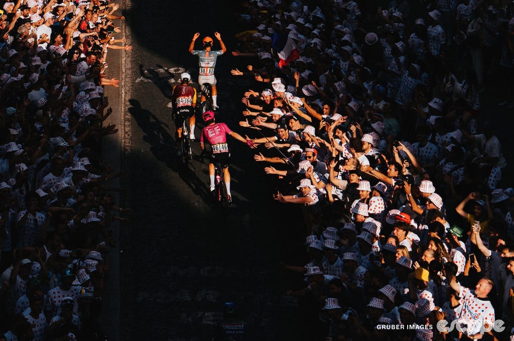 Three riders ascend through a patch of sun on the Montmartre climb on stage 21. Fans reach towards them for high-fives.