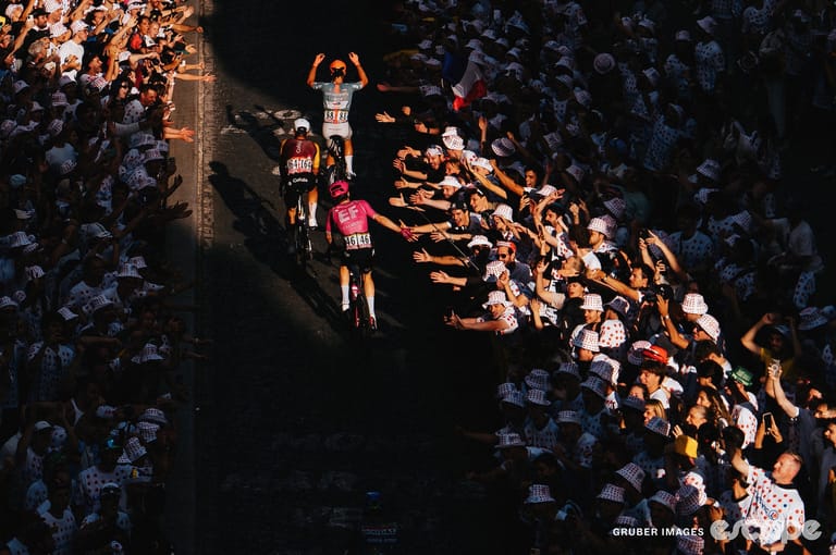 Three riders ascend through a patch of sun on the Montmartre climb on stage 21. Fans reach towards them for high-fives.