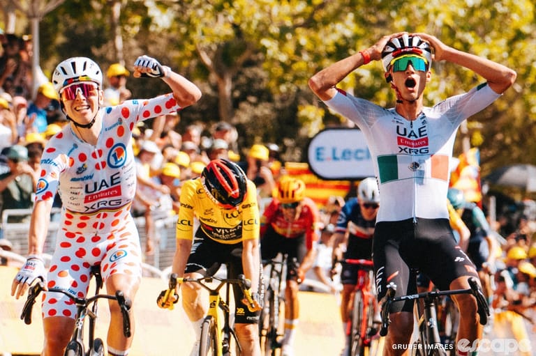 Tadej Pogačar, in full polka dots, punches the air as he and teammate Isaac del Toro (hands on head, mouth open) cross the line on stage 2 off the 2026 Tour de France.