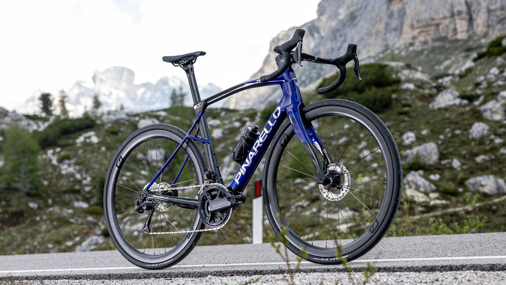 The new Pinarello X7 with a black and blue paint design along a roadside in a mountainous setting.