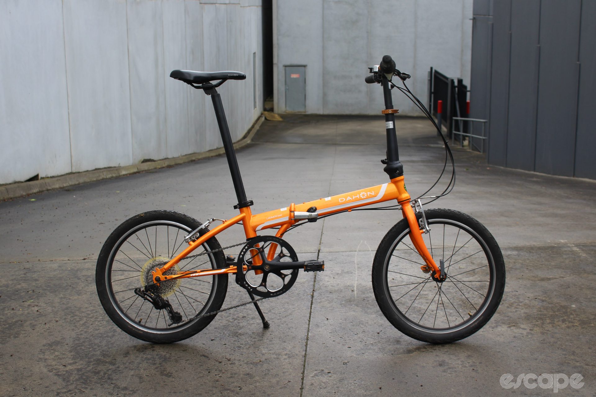 The author's basic orange folding bike, parked in a driveway.