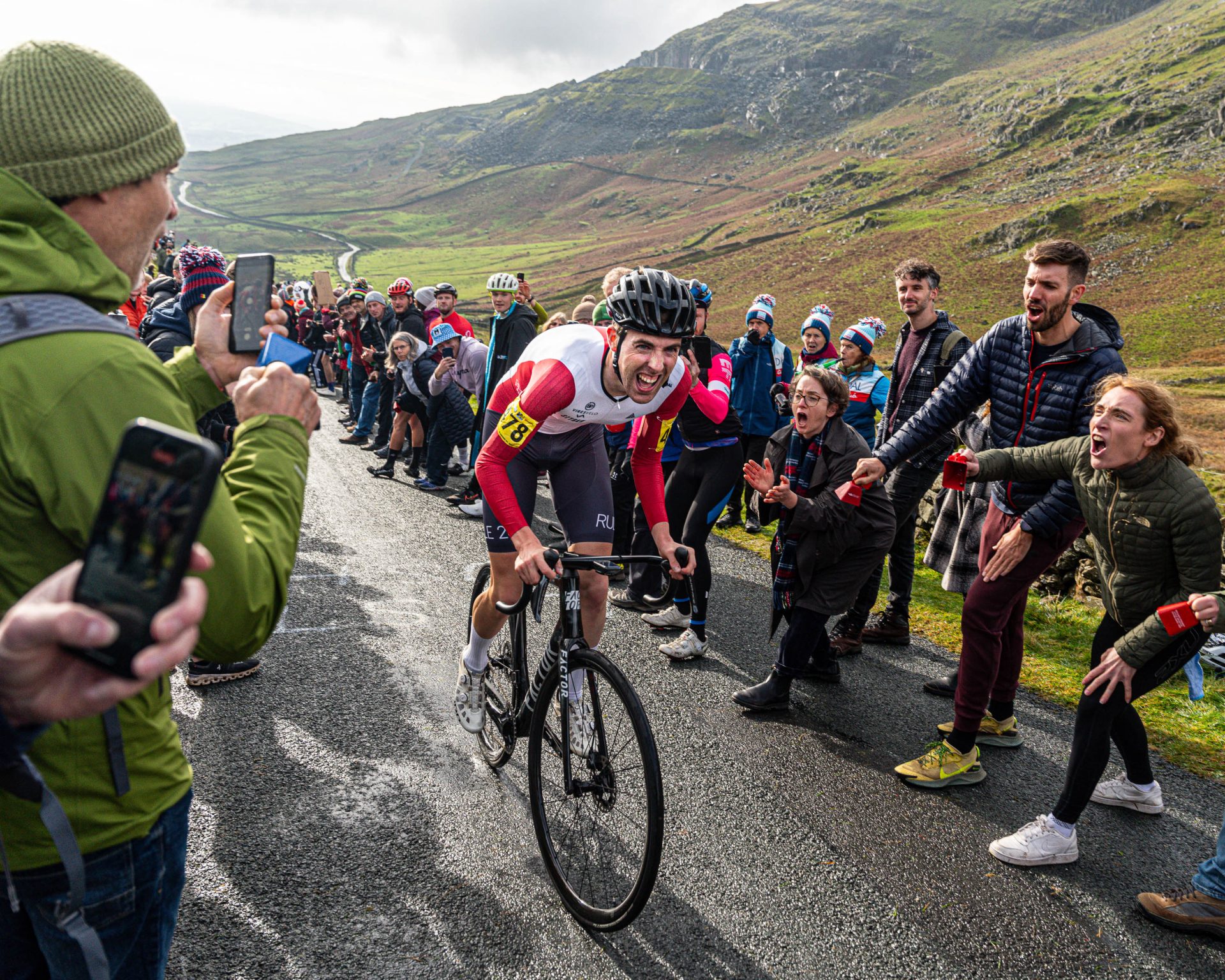 The image shows huge crowds cheering on Ed Laverack as he climbs "The Struggle" road in the 2023 British National Hillclimb championships. Laverack is grimacing with the pain of the effort.