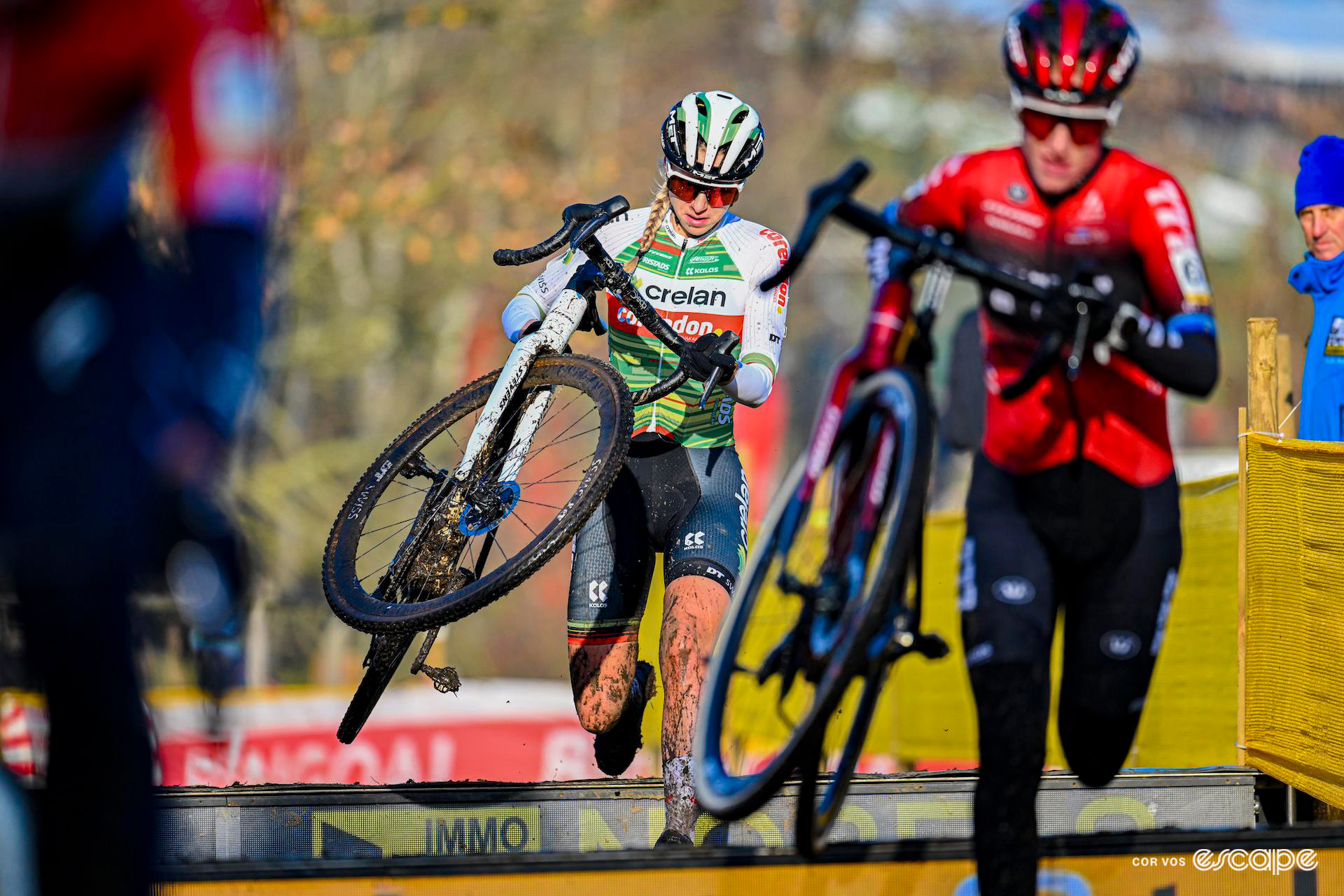 Inge van der Heijden leaps over the barriers holding her bike during Superprestige Boom, Annemarie Worst a few metres ahead of her.