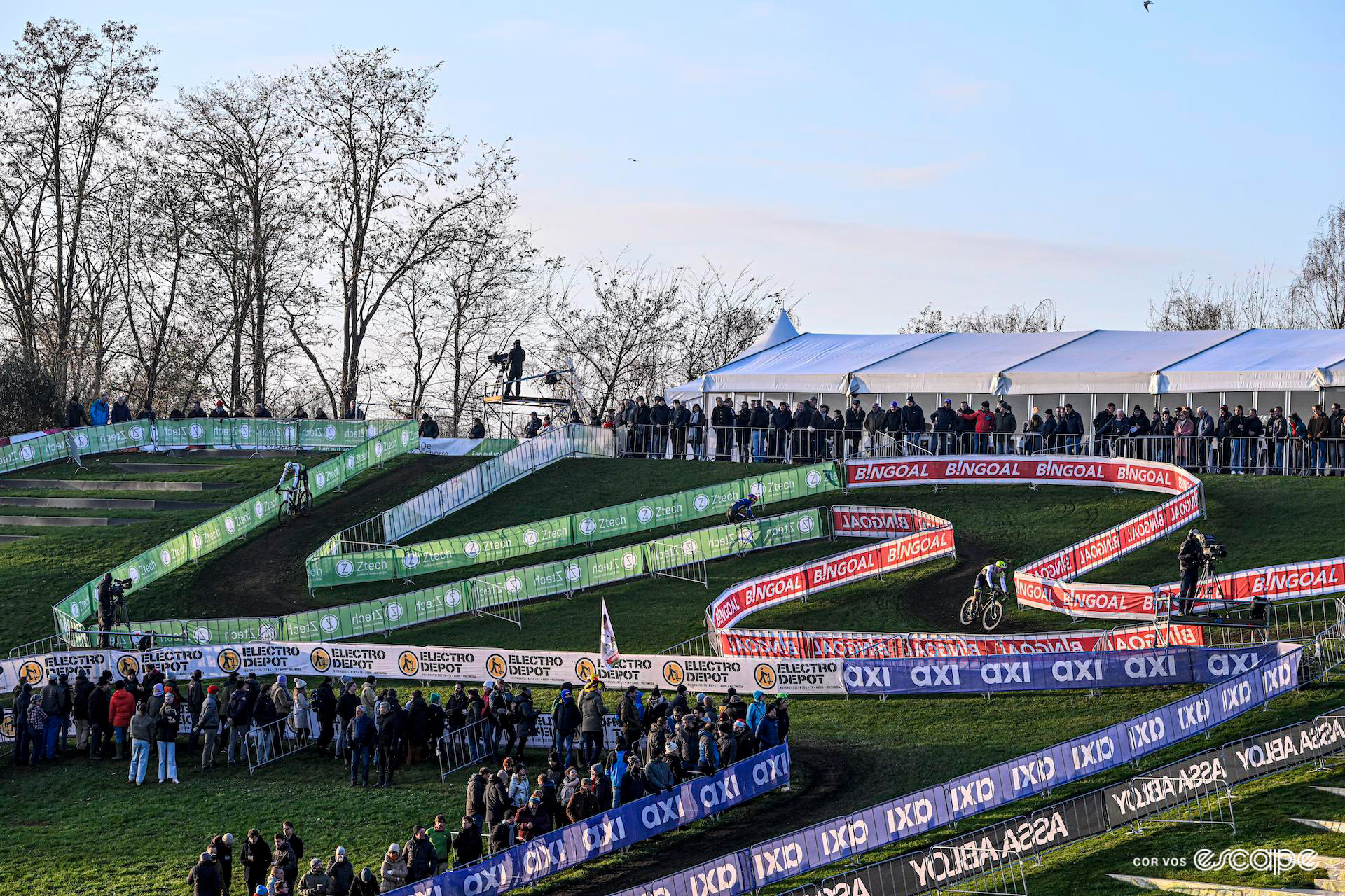 A wide shot shows snaking off-camber turns on the course as the men's field races Cyclocross Superprestige Boom.