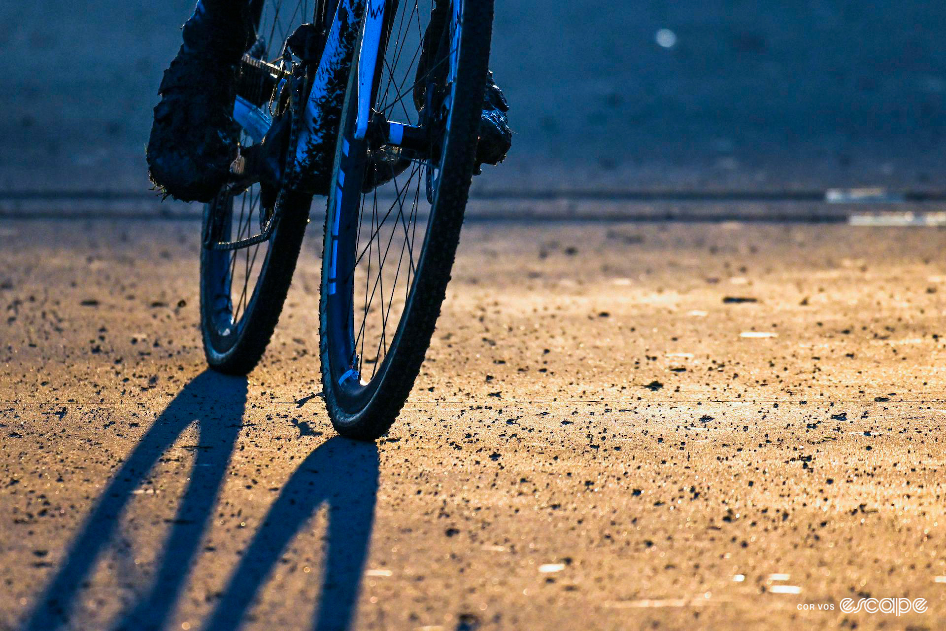 A head-on close-up of a bike's wheels and a rider's muddy shoes on the finishing straight of Superprestige Boom.