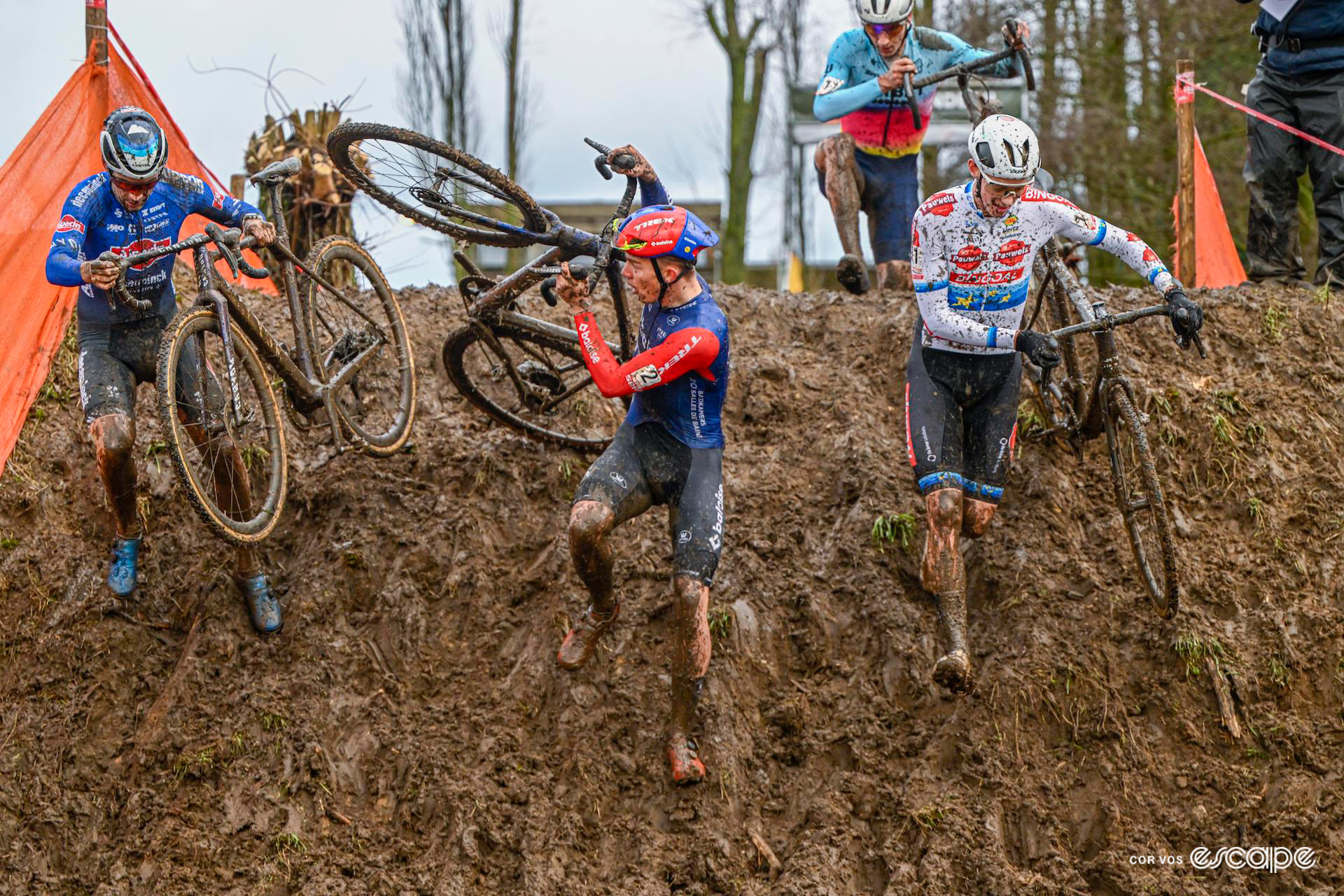 Gianni Vermeersch, Thibau Nys and Michael Vanthourenhout run with their bikes down a steep muddy ramp during Hexia Cyclocross Gullegem.