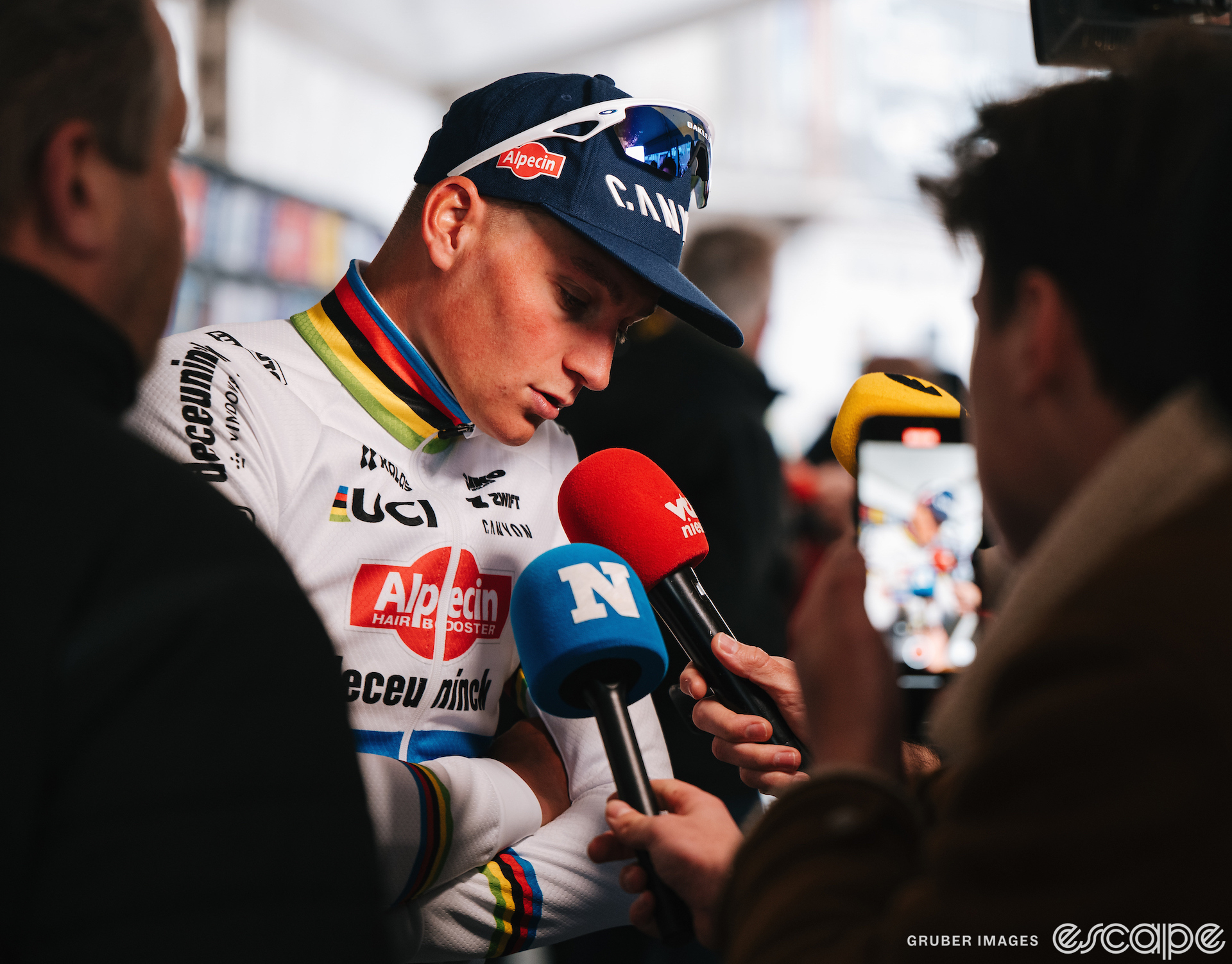 Mathieu van der Poel speaks into a pair of reporters' microphones at a race. His head is slightly bowed and he has a look of concentration on his face.