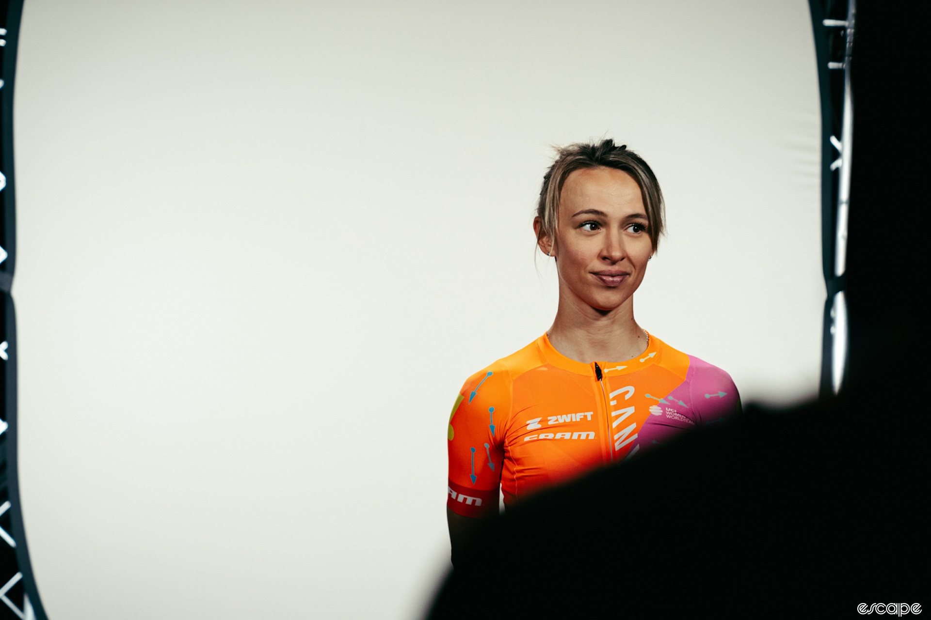 A woman in cycling clothing stands in front of a white backdrop