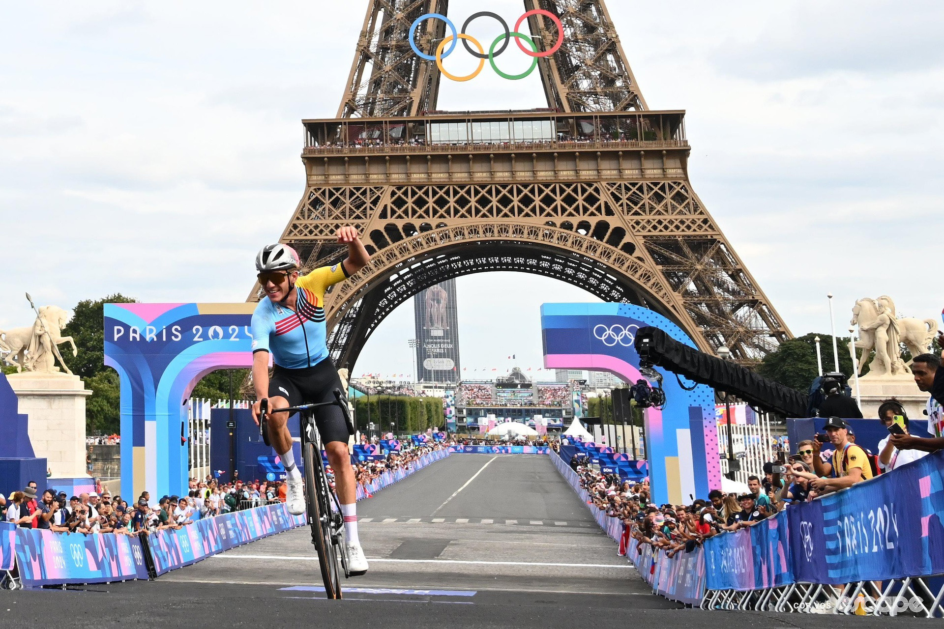 Belgian Remco Evenepoel punches the air in celebration on winning the men's Olympic road race at Paris 2024, the Eiffel Tower in the background.