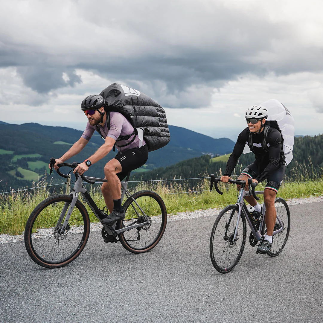 Two riders wearing RAF1 fairing backpacks ride on the road against a rural landscape.