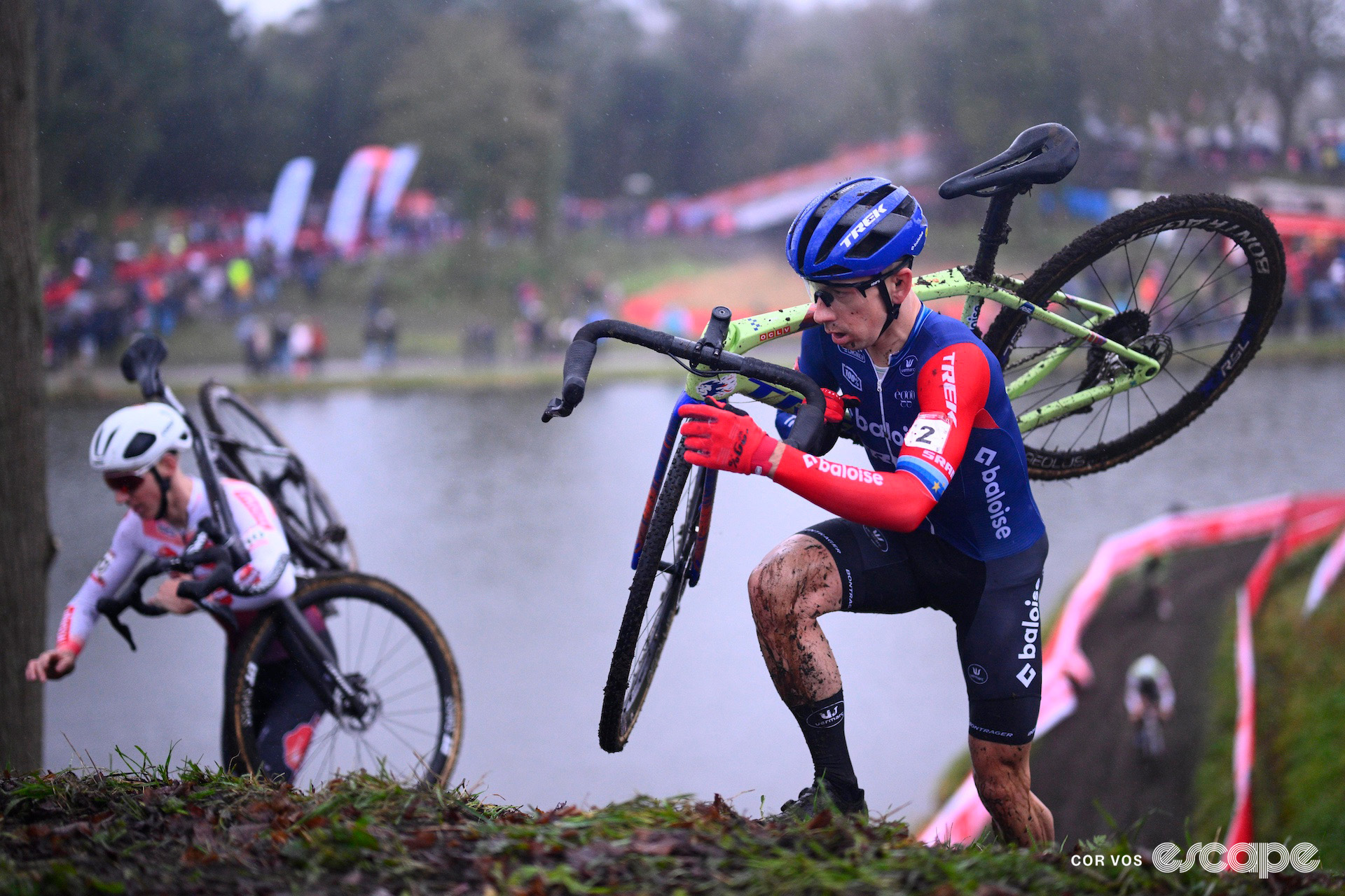 Lars van der Haar and elite men's World Cup leader Michael Vanthourenhout in the background crest the steep muddy ramp on foot with their bikes on their shoulders during cyclocross World Cup Hulst.