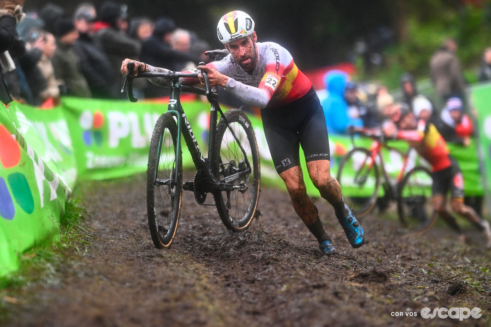 Spanish national champion runs with his bike on a muddy off-camber section during cyclocross World Cup Hulst, Belgian national champ Eli Iserbyt in the background.