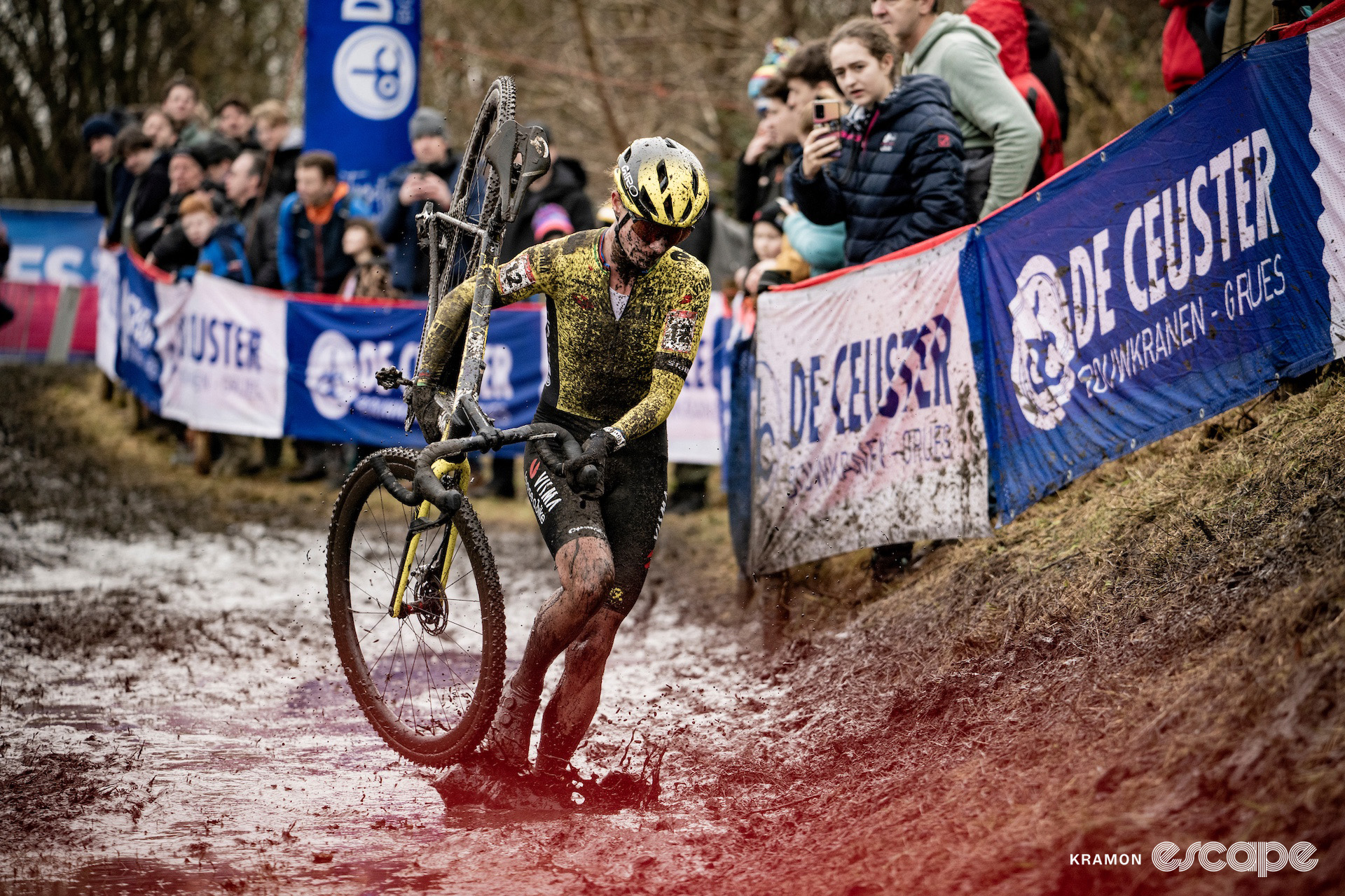 Marianne Vos in the process of lifting her bike onto her shoulder as she runs through a thick muddy puddle during cyclocross World Cup Maasmechelen.