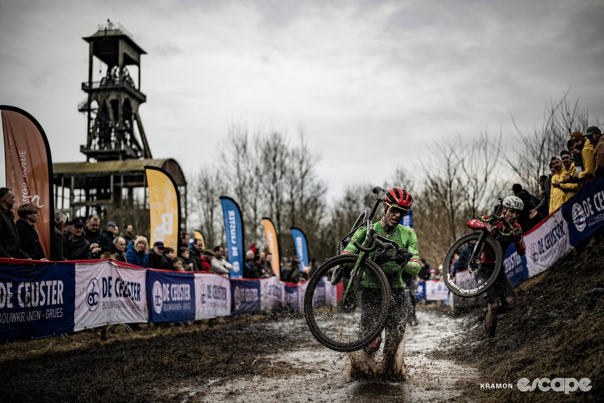 Some of the elite men splash through a deep muddy puddle, their bikes on their shoulders, during cyclocross World Cup Maasmechelen.