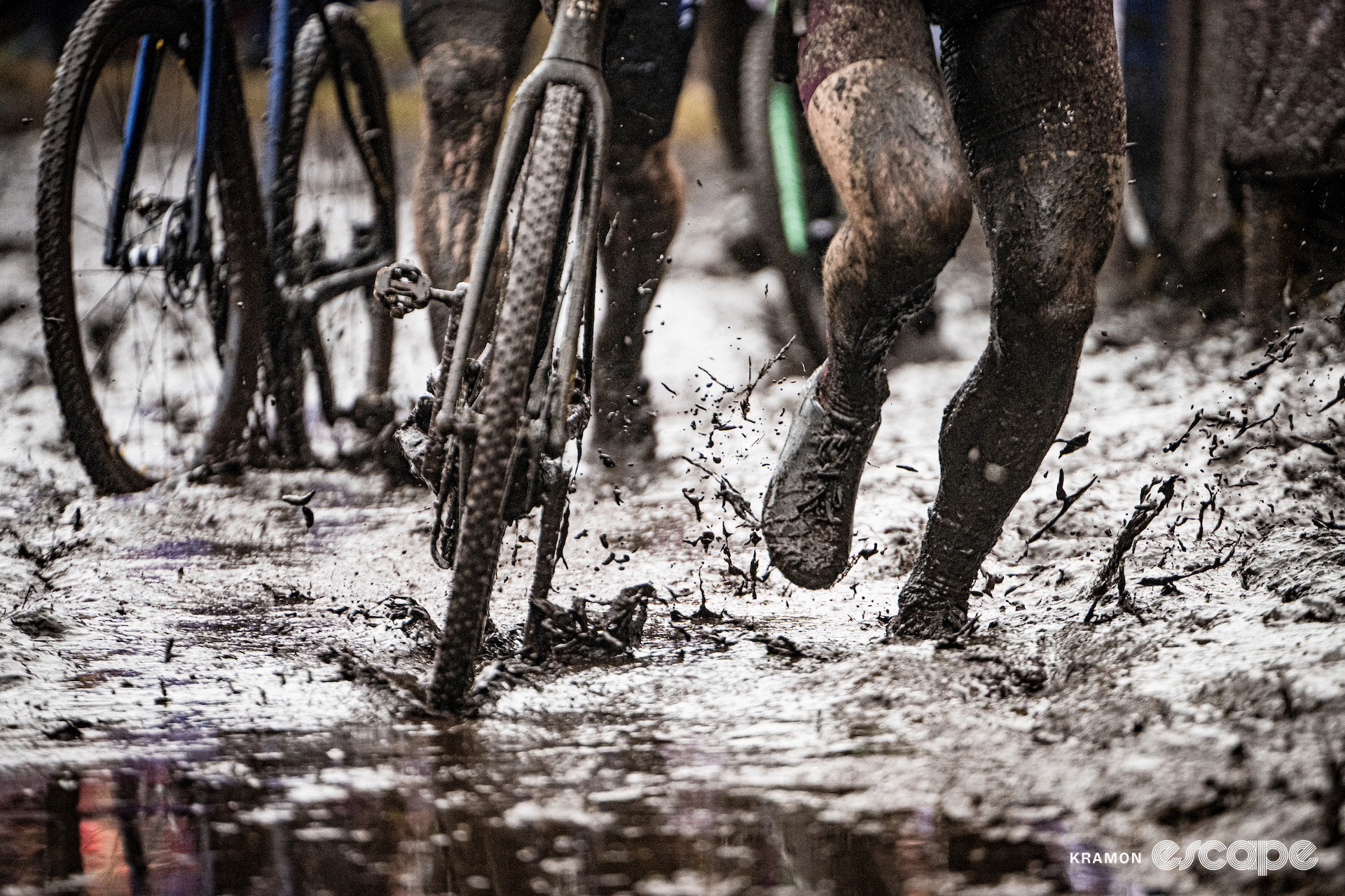 An illustration of just how muddy it was at cyclocross World Cup Maasmechelen as the legs of a few elite men run through a deep muddy puddle alongside their bikes.