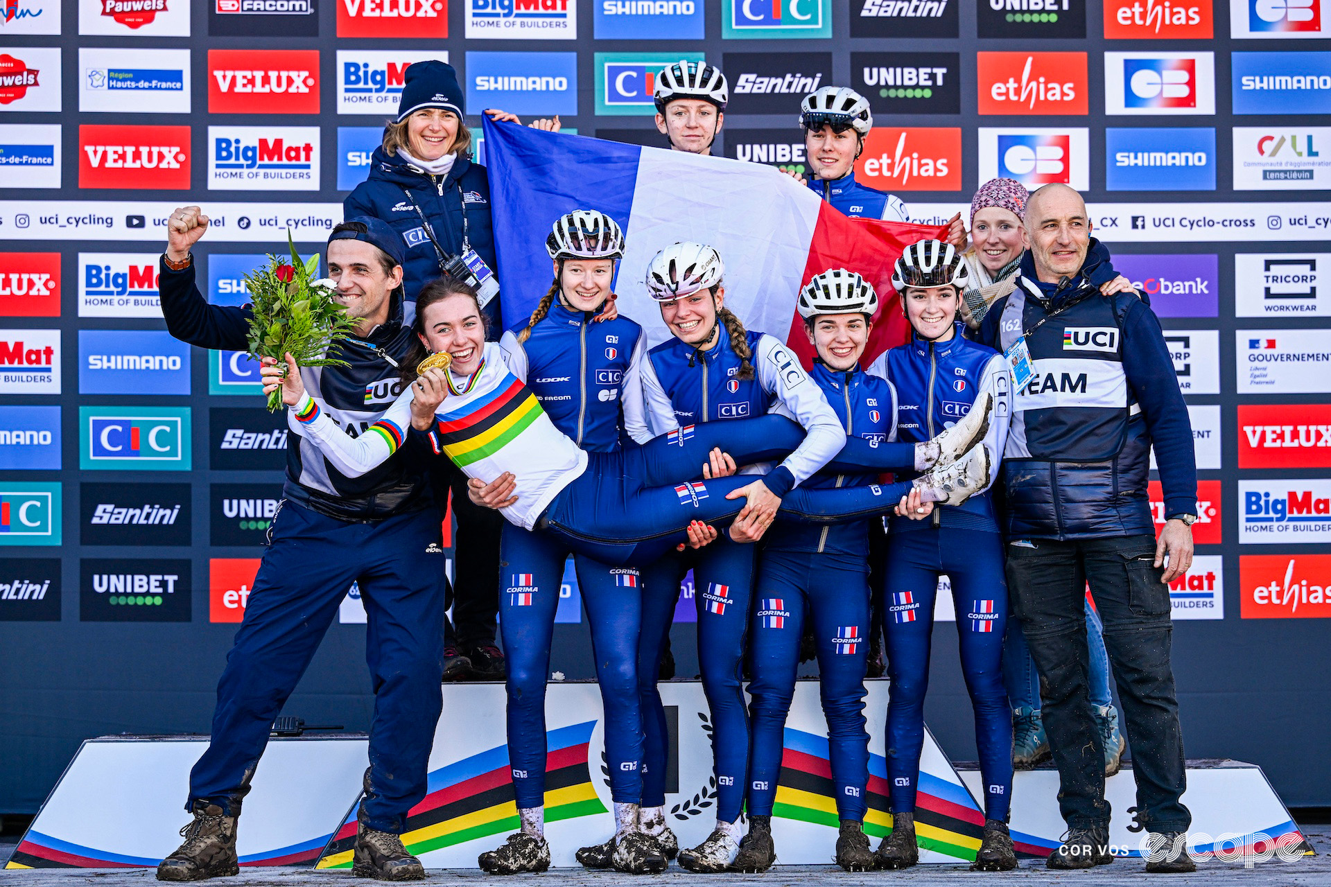 New junior women's world champion Lise Revol in her rainbow jersey being lifted up by her teammates and staff on the podium of the 2025 cyclocross World Championships.