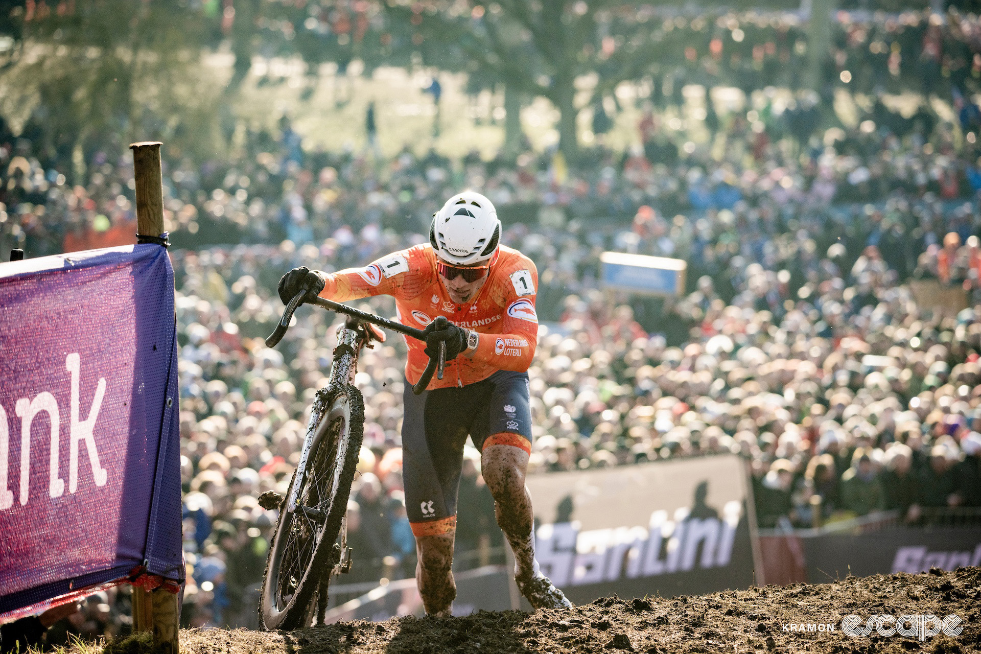 Mathieu van der Poel crests a steep ramp alongside his muddy bike during the 2025 elite men's cyclocross World Championships.