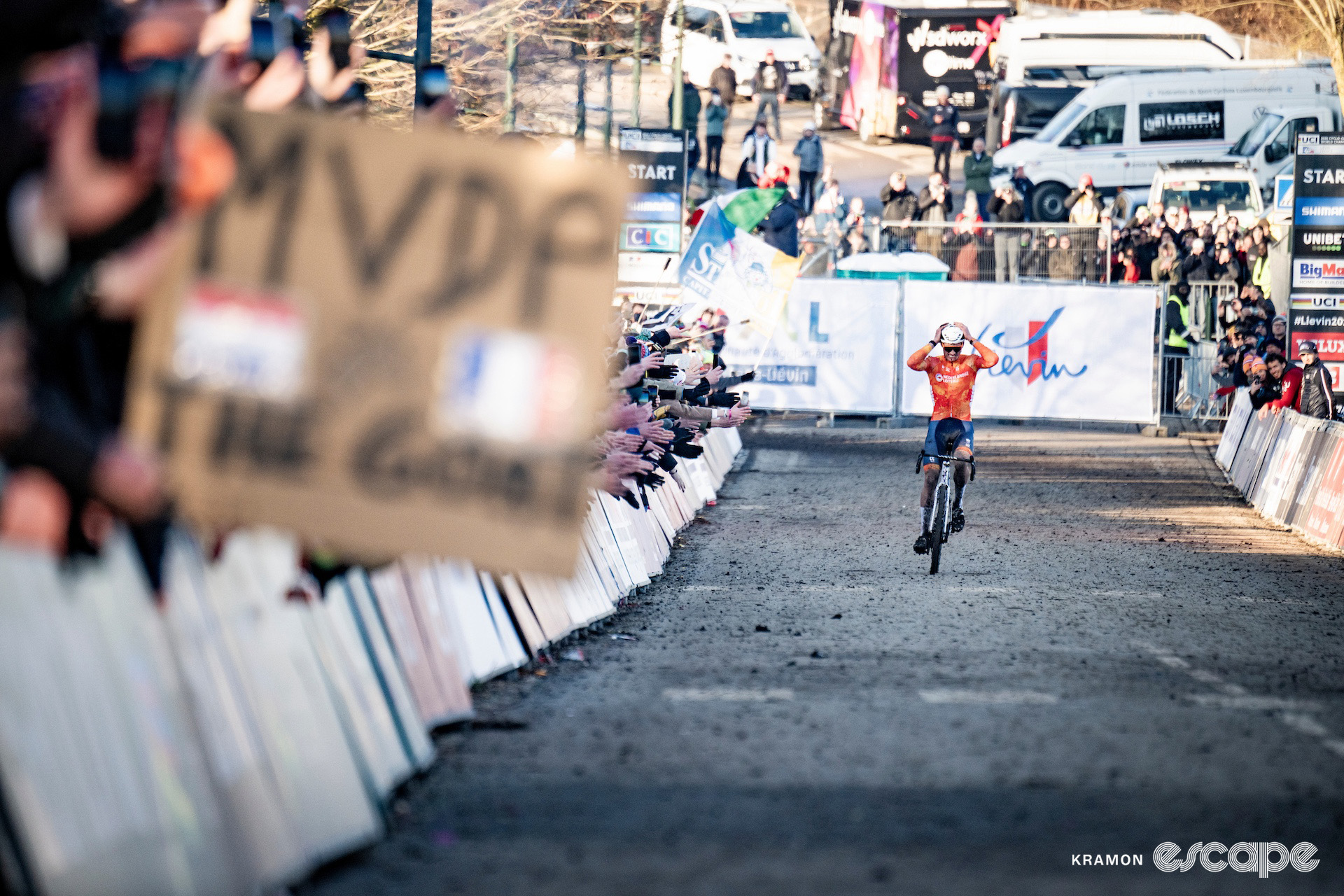 Mathieu van der Poel rides up the finishing straight at the 2025 elite men's cyclocross World Championships, a blurry sign in the foreground that reads "MVDP the goat."