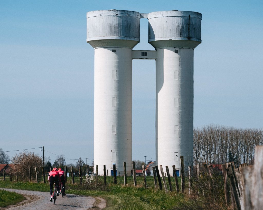 Two white water towers loom over a pair of pink-clad EF racers as they navigate the race's longest sector of cobbles, Hornaing à Wandignies.