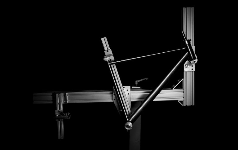A frame in the process of being built is shown in this black-and-white photo. The front triangle is attached to a welder's jig.