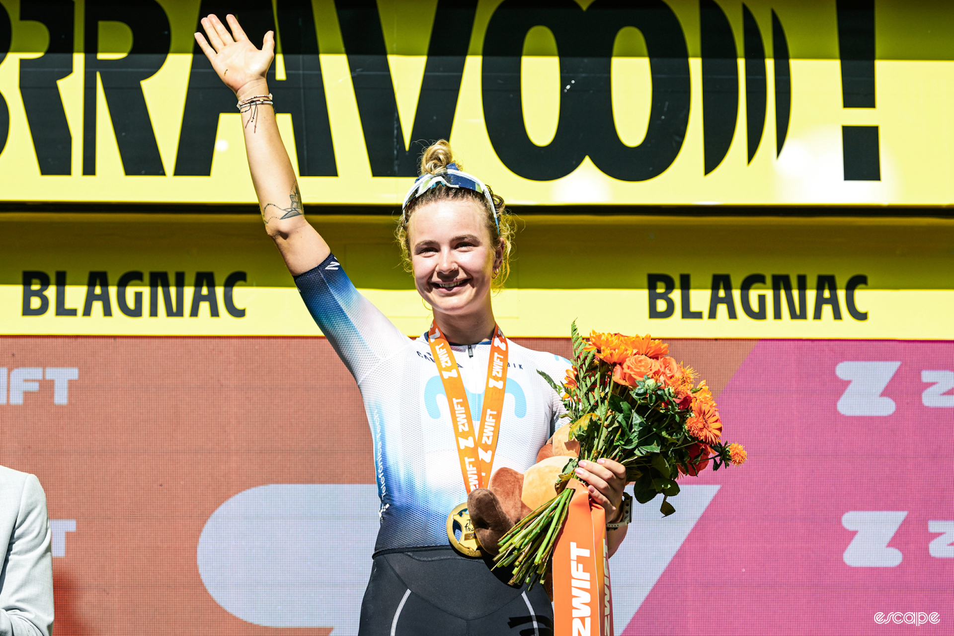 A smiling Emma Norsgaard waves from the podium after winning the sixth stage of the Tour de France Femmes.