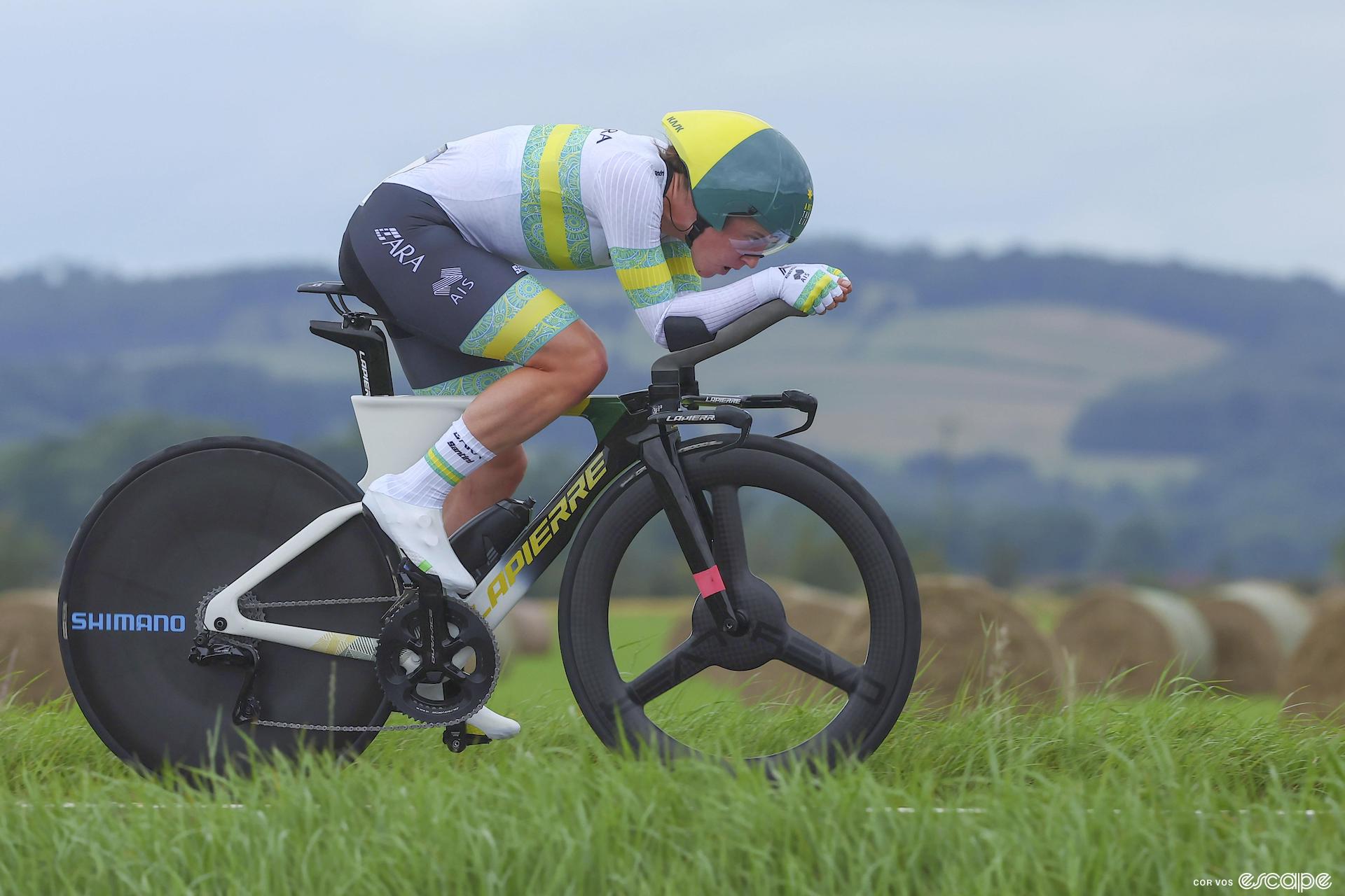 Grace Brown rides in the 2023 World Time Trial Championship in Glasgow, Scotland. The Australian is dressed in the national team kit, with green and yellow bands, and is in an extremely aerodynamic position en route to her second consecutive silver medal.
