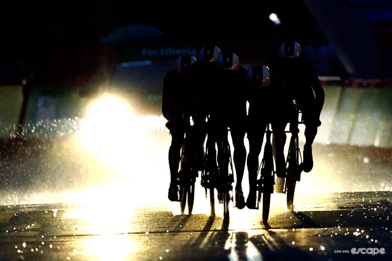 Soudal-Quick-Step's riders in the dark, backlit by a follow-car's lights.