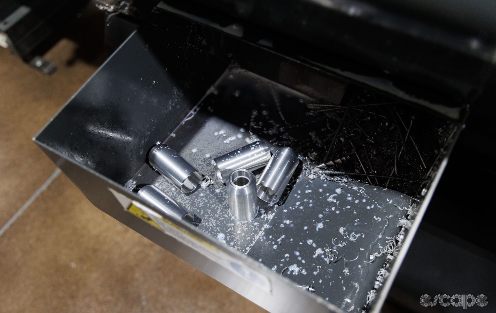 Machined parts of the Star Nut Setter sit in a tray below the machine, sitting in a pile of what look like very sharp metal shavings.