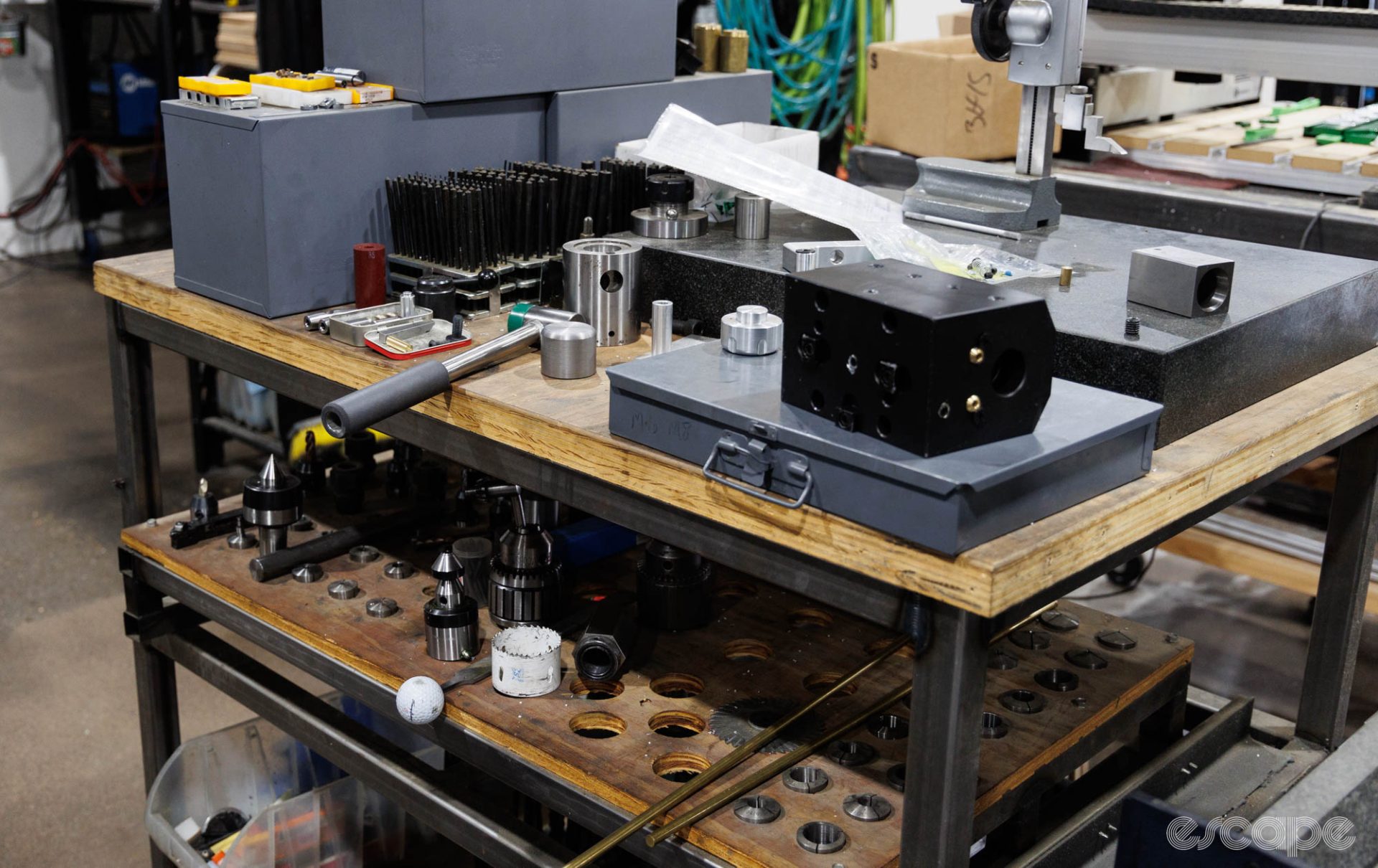 A number of milling tool attachments sit on a low bench, tucked under a waist-height bench with a hammer and miscellaneous other tools.