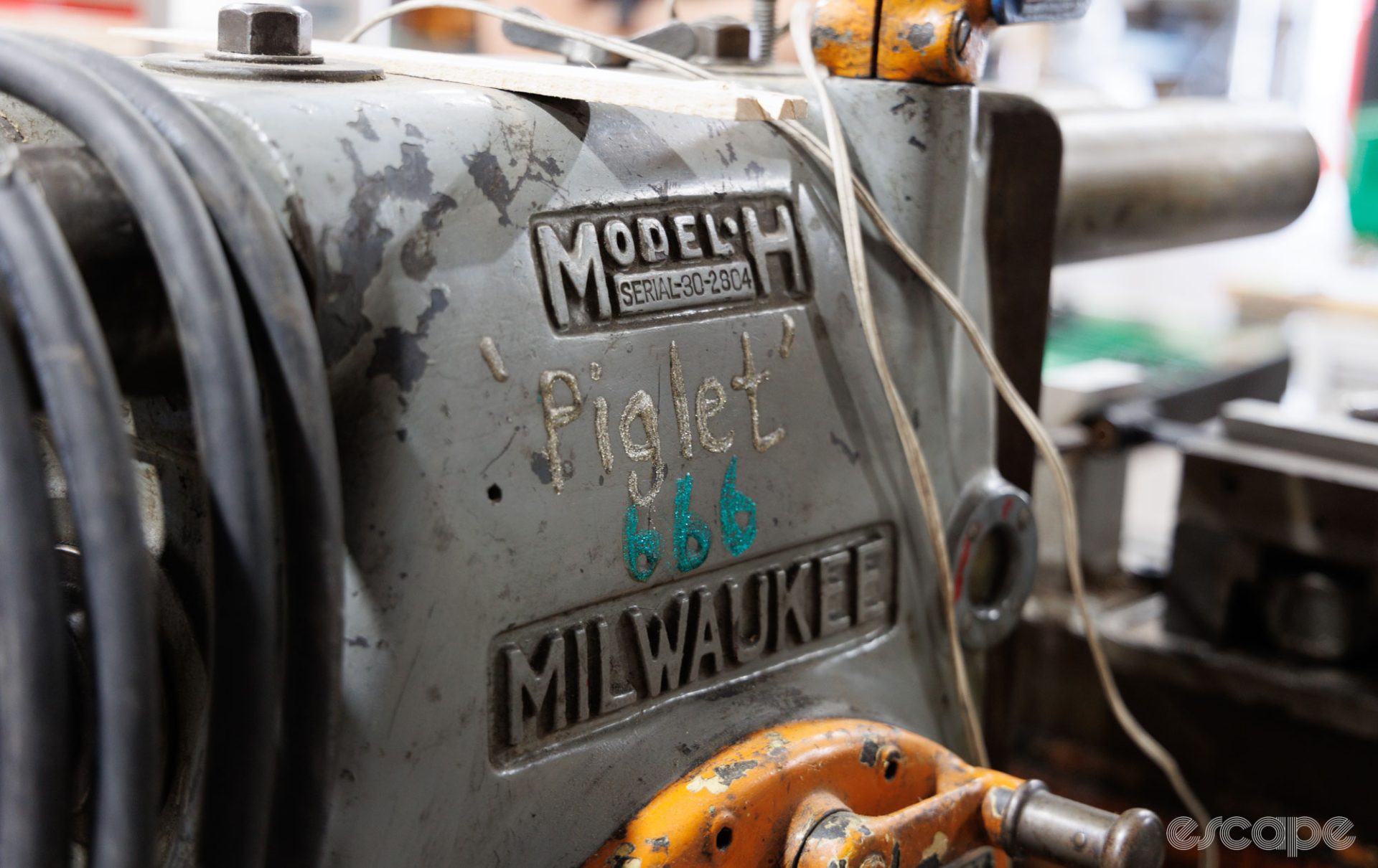An ancient horizontal mill is shown in close-up. The Milwaukee Model H has obvious signs of long use and the name "Piglet" inscribed in thick silver paint above the numbers "666" in turquoise.