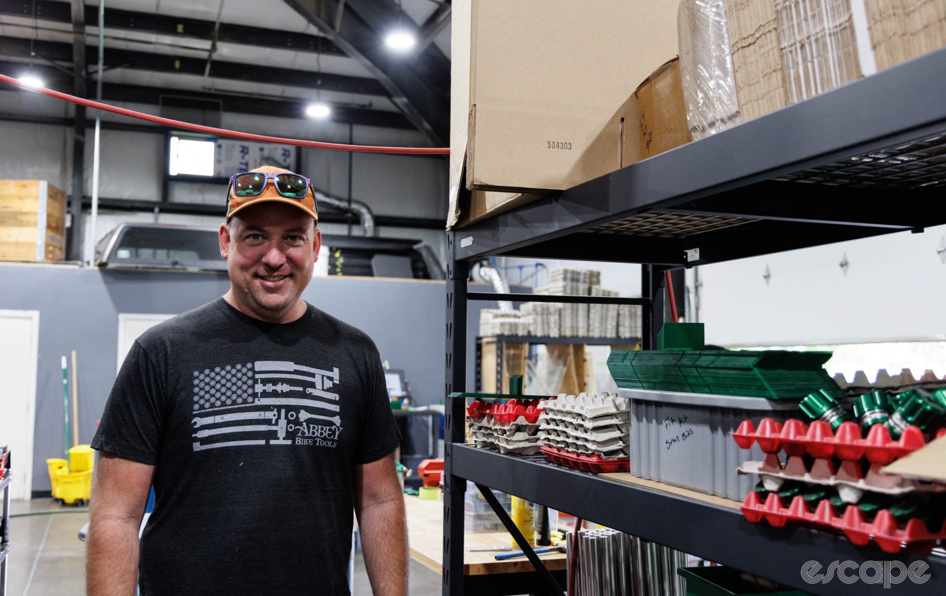 Abbey founder Jason Quade stands near a shelf of tool parts. He's wearing a black t-shirt with an American flag-style design made of Abbey's tools.