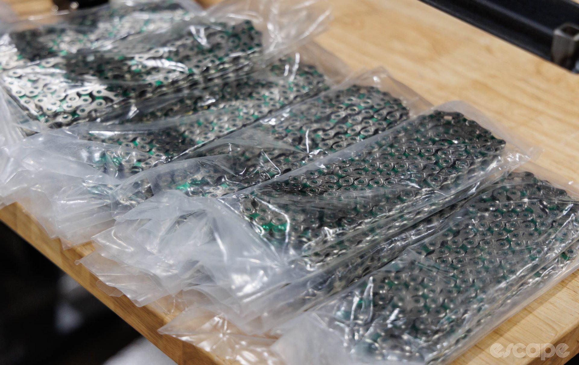 Stacks of KMC chains sit in plastic bags on a bench. The inner links are Abbey's green color.