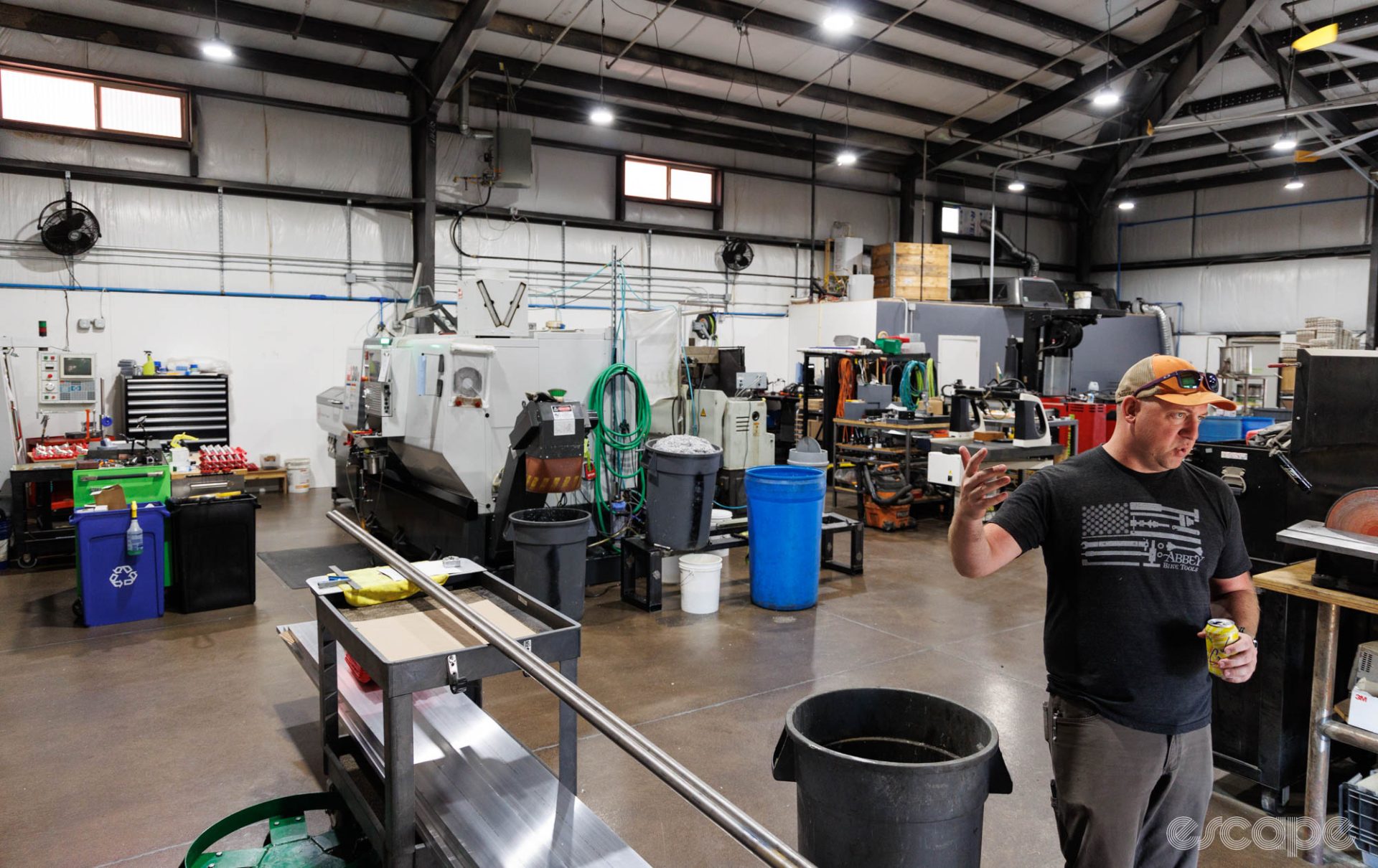 Jason Quade stands on the shop floor, which is compact and packed with machine tools under a tall ceiling. High windows let in some natural light.
