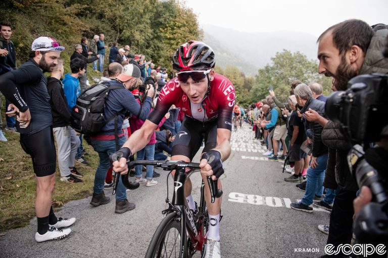 Tao Geoghegan Hart races toward the camera at the 2019 Tour of Lombardy. He's alone, on a narrow road lined with fans, and his mouth is open as he gives chase.