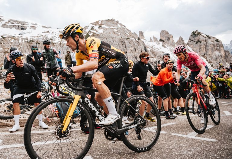 Primoz Roglic leads Geraint Thomas, who is in the pink jersey, up a large climb with snow capped peaks in the background at the 2023 Giro d'Italia.