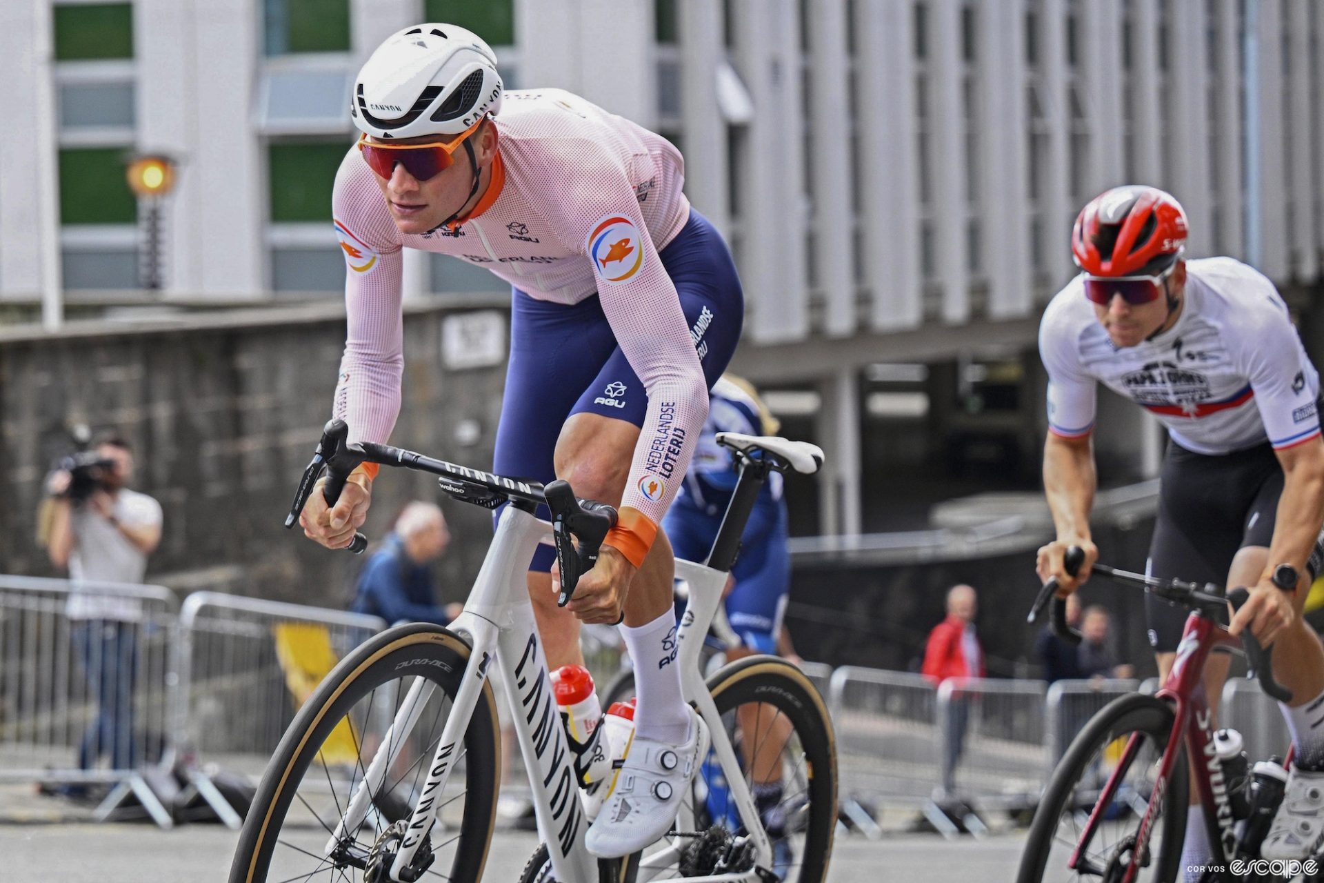 Dutch rider Mathieu van der Poel rides the Glasgow World Championships road course in training, pedaling up a short, steep climb out of the saddle while dressed in a white long-sleeve jersey and blue shorts.