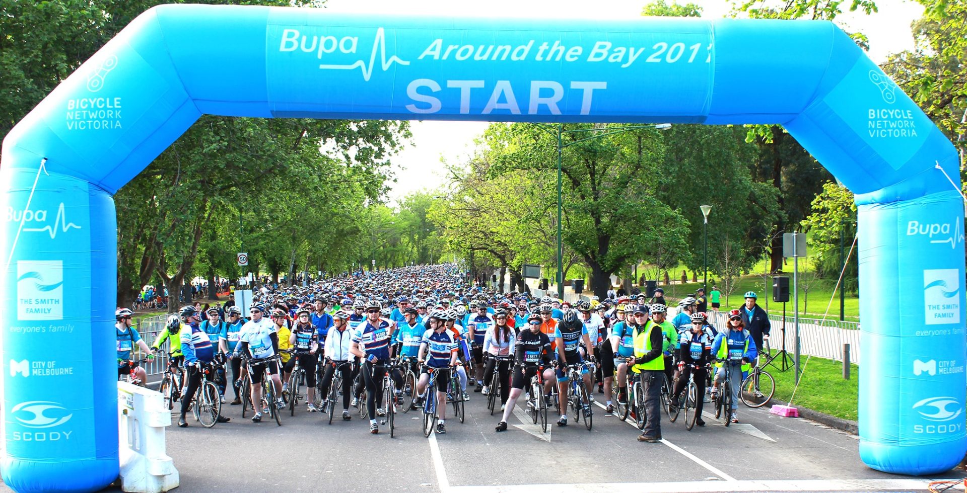 A mass of cyclists await the start of the 2011 Around the Bay under a blue event gantry bearing the name of the event.