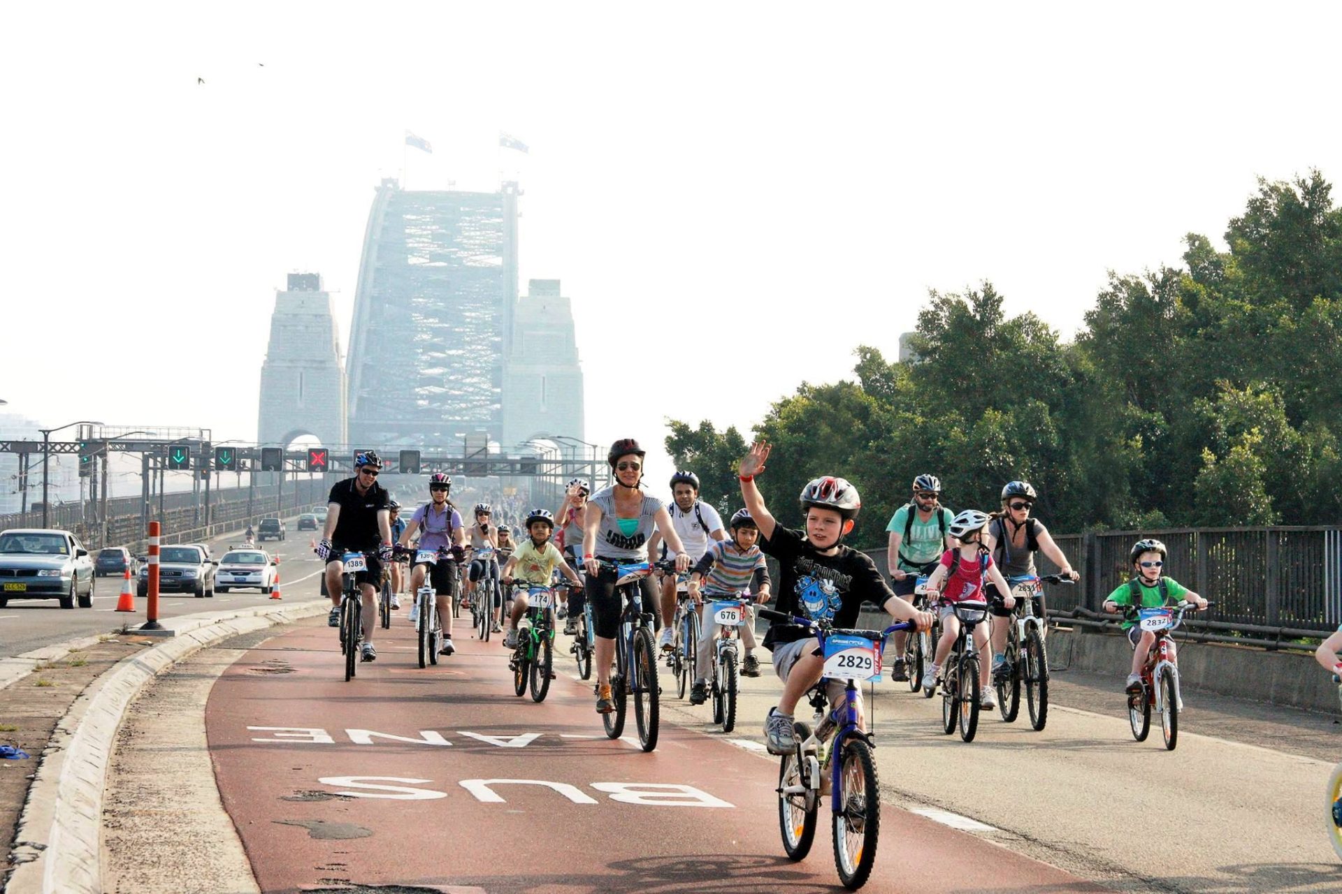 A group of cyclists, of all ages, ride on a closed road with the Sydney Harbour Bridge in the background.
