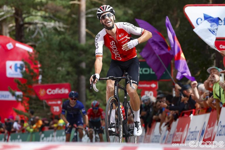 Jesus Herrada of Cofidis crosses the finish line alone on stage 11 of the 2023 Vuelta a España. The Cofidis rider is smiling a big smile and slapping his chest with his left hand.