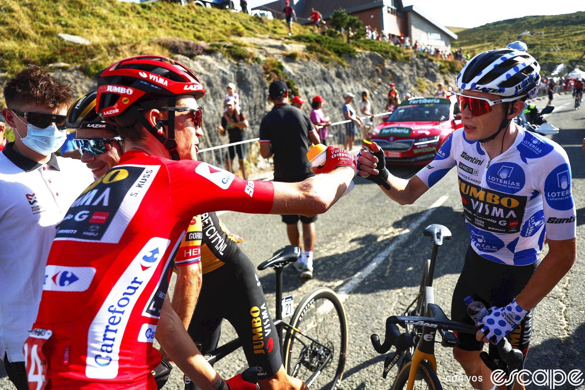 Sepp Kuss exchanges a fist-bump with Jonas Vingegaard after stage 14 of the 2023 Vuelta a España. Kuss is in the red jersey of race leader, while Vingegaard is in the white with blue polka dots of best climber. Kuss is smiling, while Vingegaard has a slightly more neutral expression.