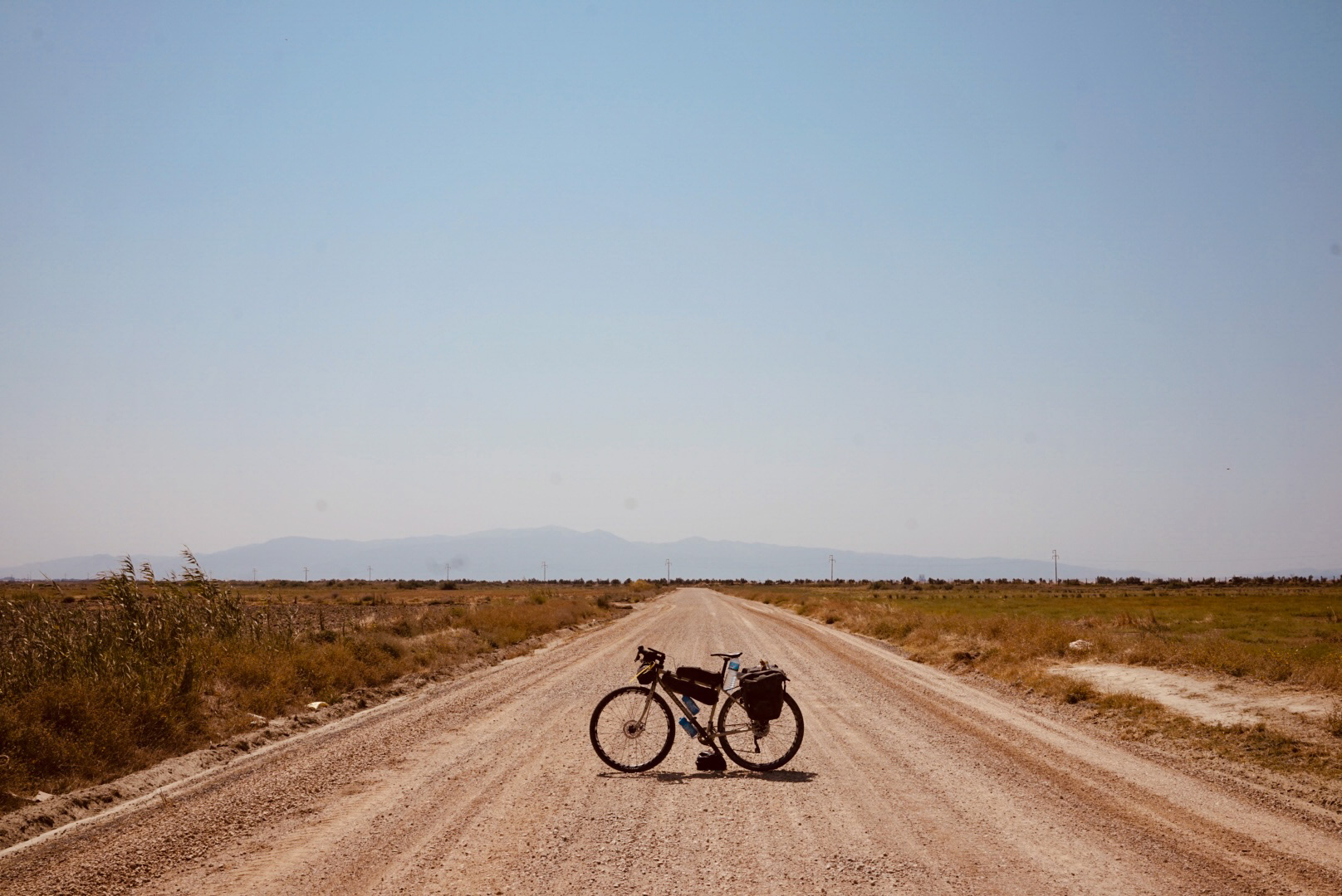 Mattia Lazzarin's bike stands in silhouette on a long gravel road stretching off to the horizon. 