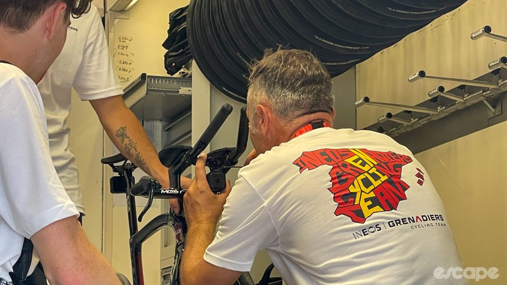 The photo shows a team mechanic mounting a GoPro camera to the front of a tt bike.