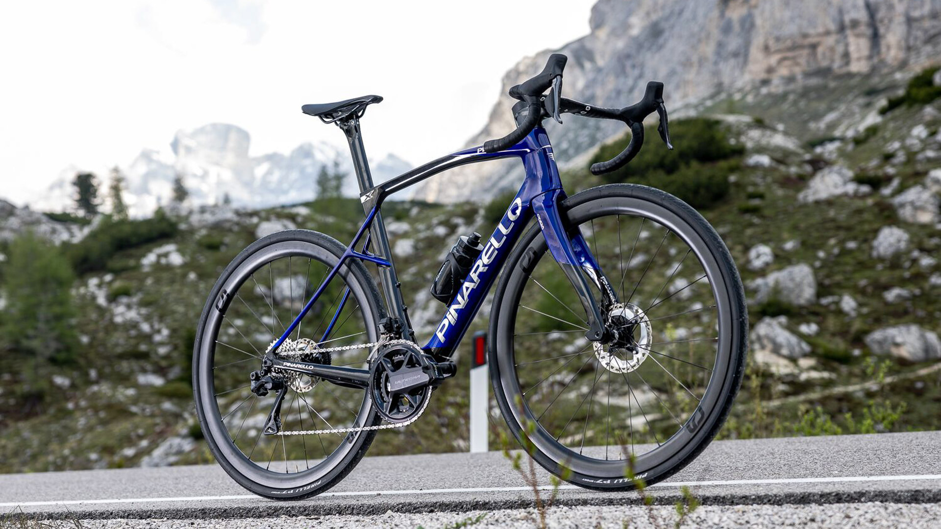 The new Pinarello X7 with a black and blue paint design along a roadside in a mountainous setting. 