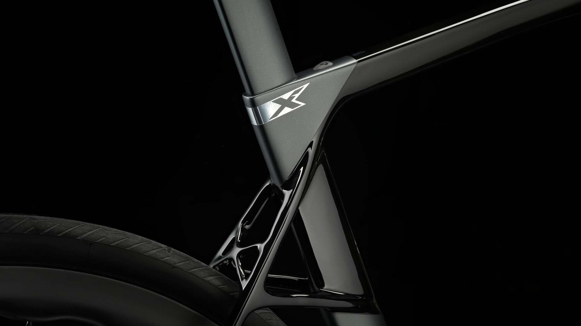 The seat tube and seat stay intersection area on the new Dogma X. The new X logo on the side of the seat tube near the top is central in the image, but the image also shows the new dual attachment configuration of the seat stays and the X-bridge connecting the two independent seat stays. 
