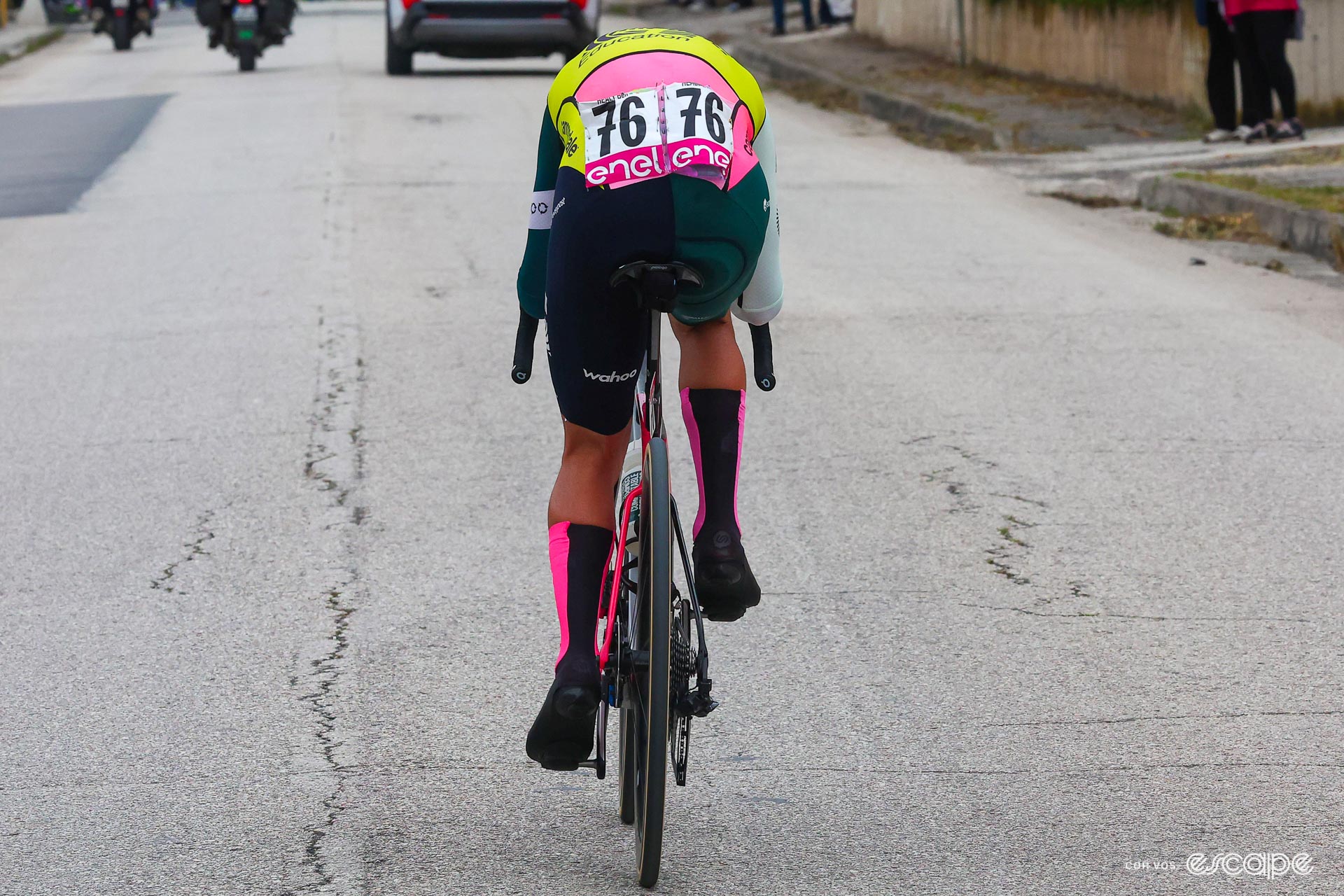 A cyclist adopting an aerodynamic racing position viewed from the rear. The rider's head is entirely hidden from view by his torso, highlighting the benefits in terms of reduced frontal area by the cyclist's decision to dip his head as low as possible. The cyclist is Ben Healy of the EF Education-EasyPost team racing at the 2023 Giro D'Italia. 