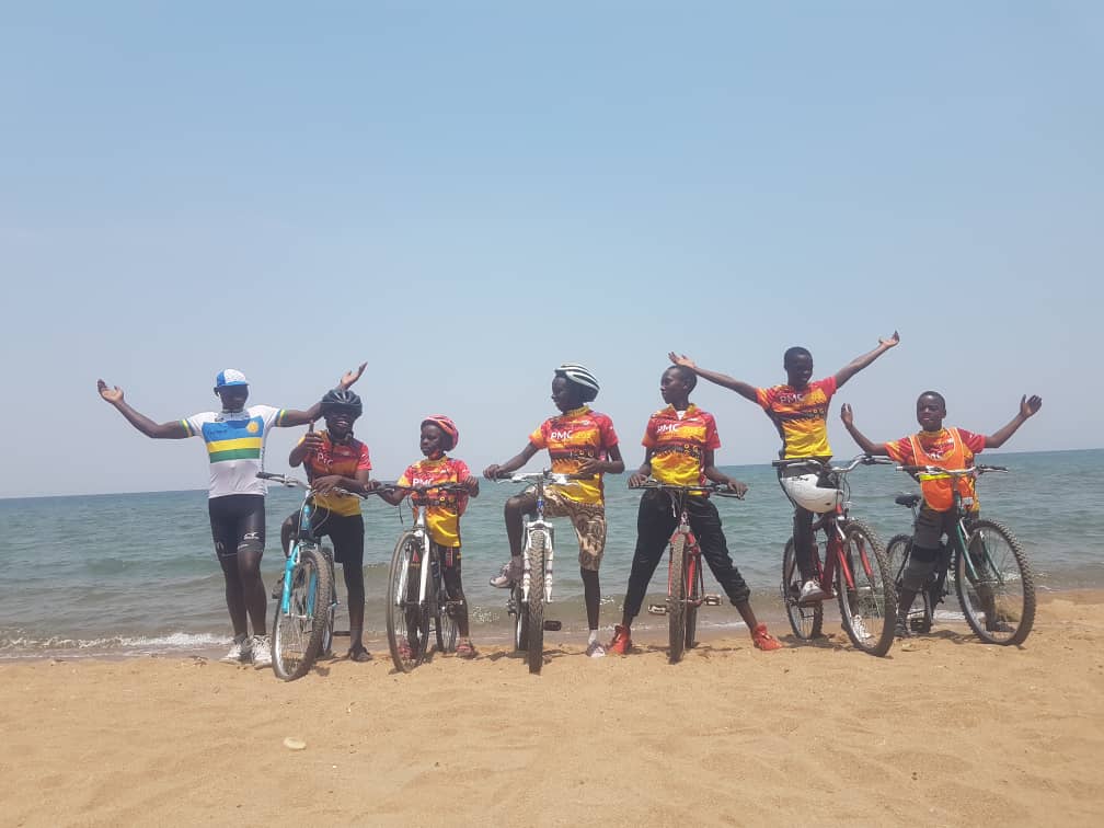Gasore Hategeka with his team of young cyclists, all of them visibly happy, some of them raising their arms. 