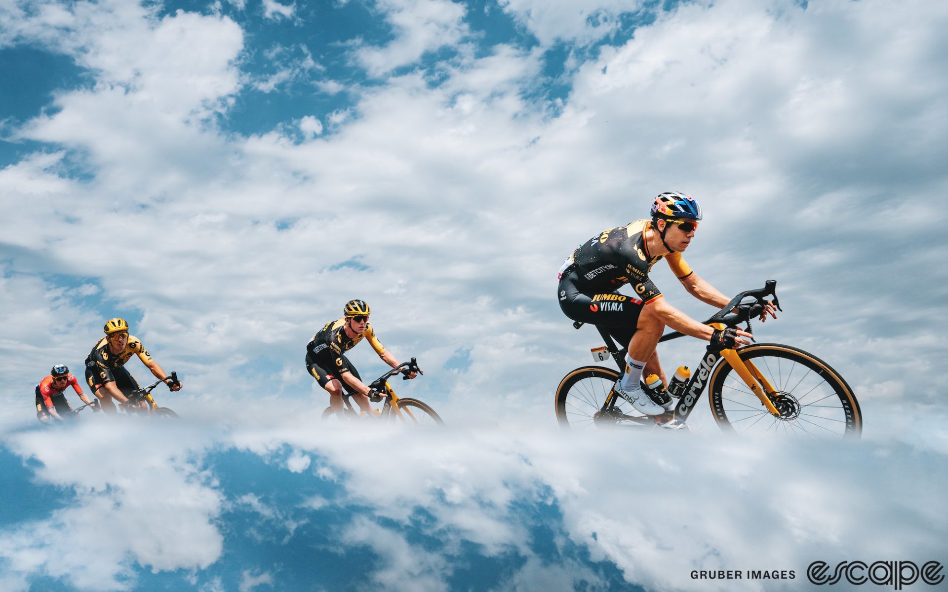 Wout van Aert leads Jumbo riders on a descent at the 2023 Tour de France. He's arcing around a corner under a blue sky with white-and-grey clouds, reflected in the bottom third of the image in a compositional creation.